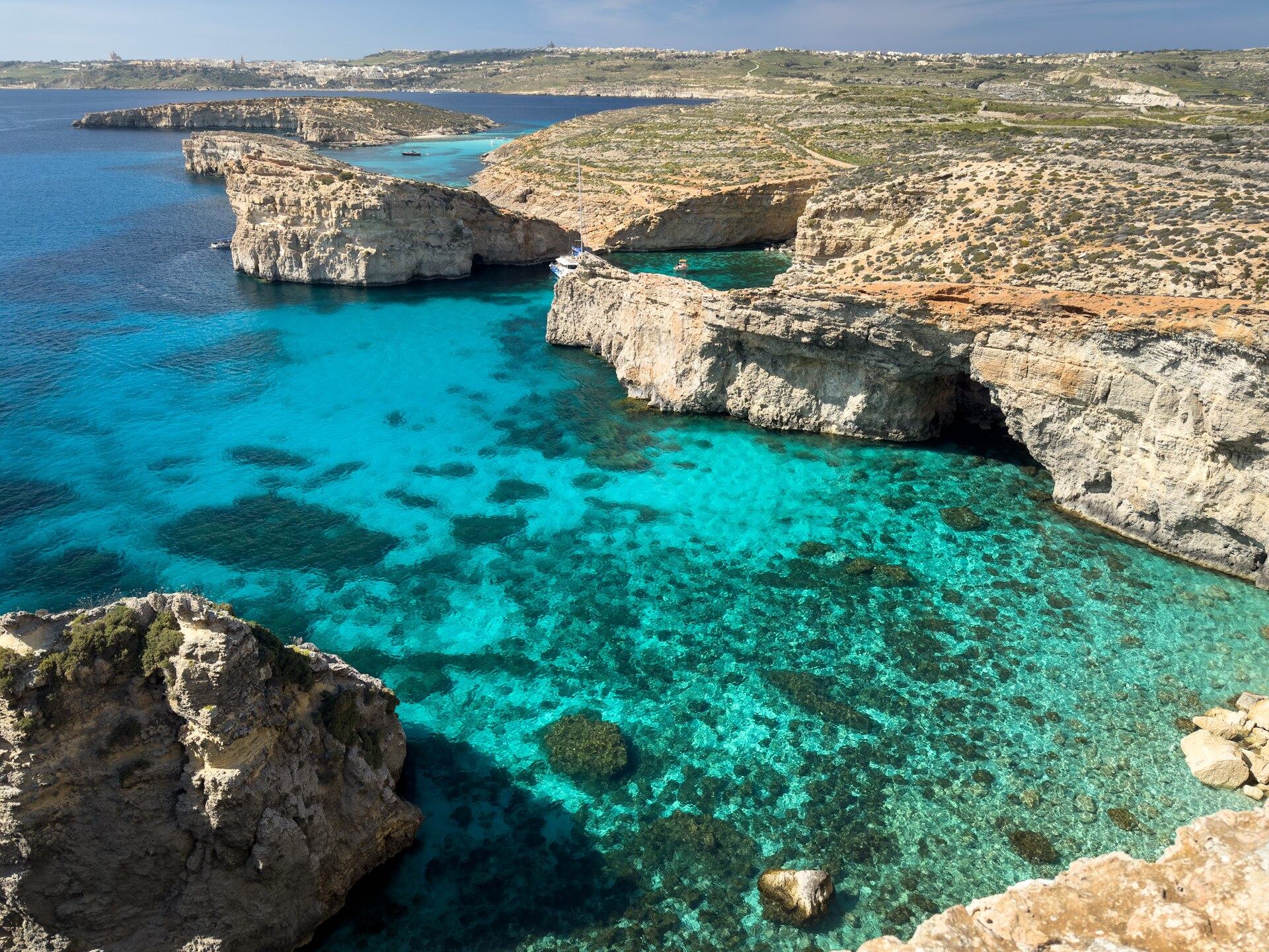 Bright turquoise water enclosed by low limestone arms on the Comino coast